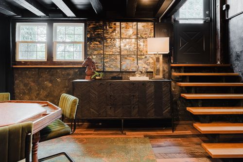 Dark herringbone-front sideboard with a table lamp beside open wood stairs