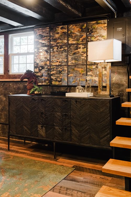 Dark chevron-front media console with abstract wall art panels and open stairs