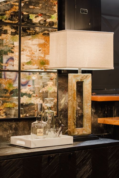Side table vignette with liquor decanters and a stone-base lamp against art panels