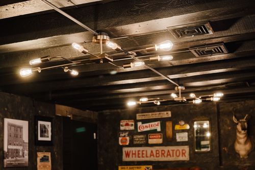 Brass sputnik-style pendant lights on a black beamed ceiling above vintage tin signs
