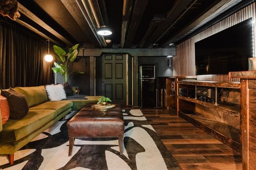 Media room with an olive green sectional, leather ottoman and wall-mounted TV