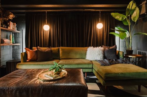 Olive green sectional sofa with mixed throw pillows beside a leather ottoman