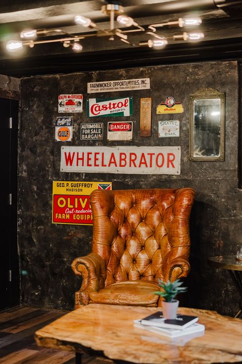 Tufted leather wingback chair beside a live-edge coffee table under vintage tin signs
