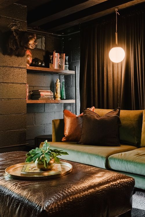Olive velvet sectional and leather ottoman beside open shelving and mounted taxidermy