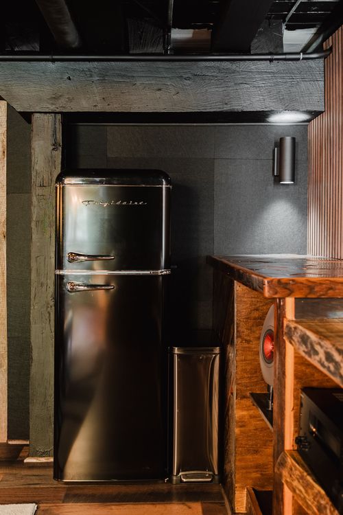 Retro black refrigerator built into a wood-paneled wet bar nook