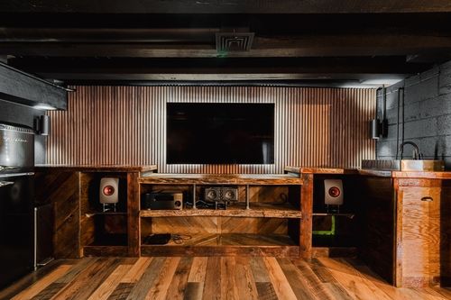 Wood wet-bar console with built-in speakers below a TV on corrugated metal paneling