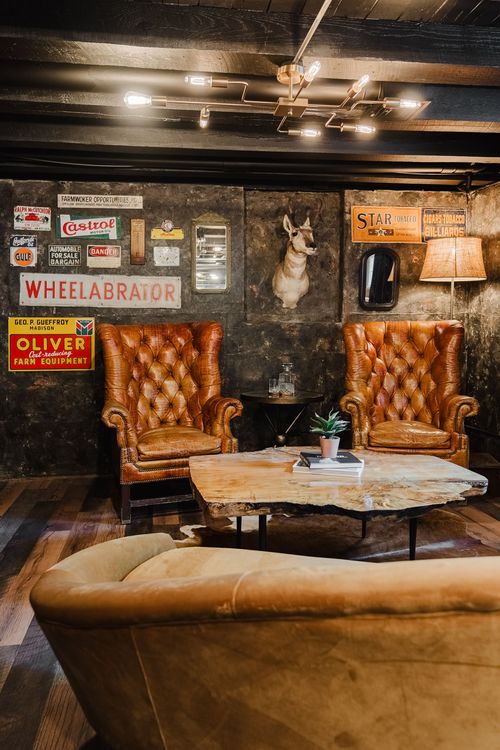 Vintage tin advertising signs and an antique mirror above a tufted leather chair