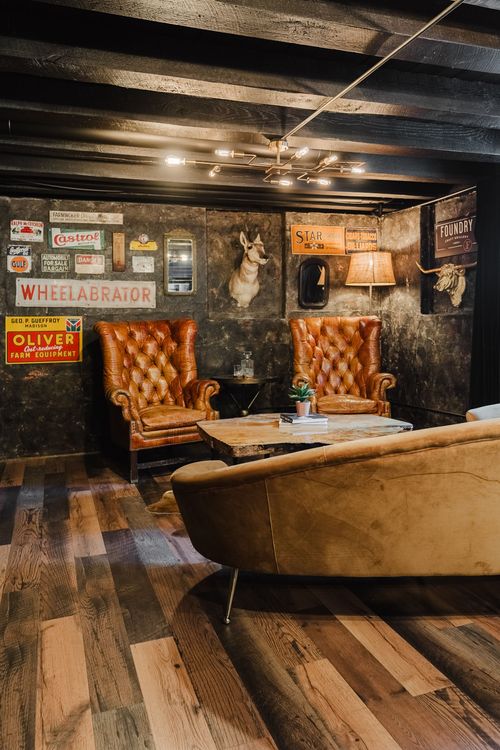 Two tufted leather wingback chairs flank a live-edge table below a mounted animal head