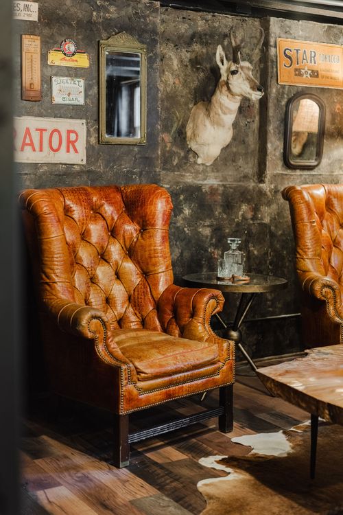 Tufted leather chair beneath a mounted antelope head and vintage tin signs