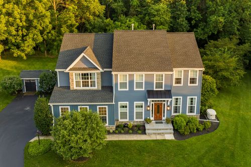 Aerial view of a blue colonial with stone accents, a tan roof and detached garage