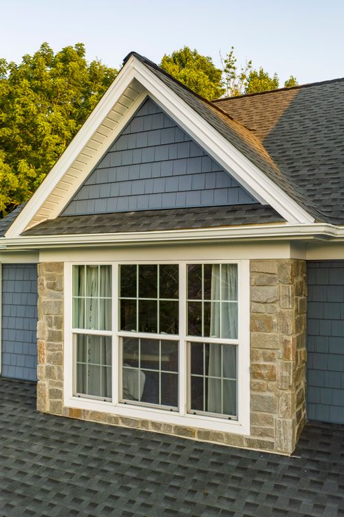 Close-up of a gabled dormer with a stone base and paned window on shingle siding