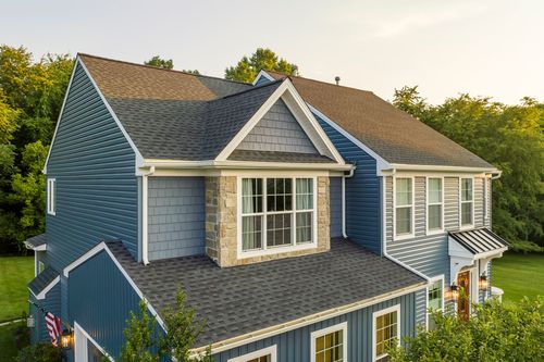 Aerial view of a blue colonial with a stone-clad bay window and three-car garage