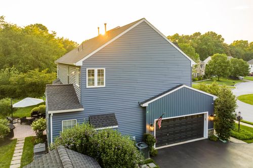Aerial view of a blue two-story home with a black garage and shaded patio