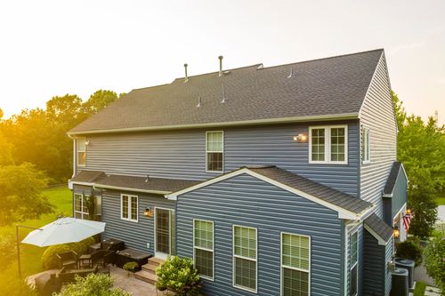 Aerial view of a blue colonial rear elevation with patio furniture and dormers