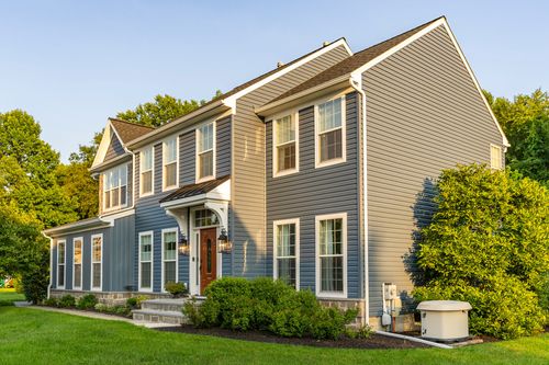 Front elevation of a blue-gray colonial with a stone base and covered entrance