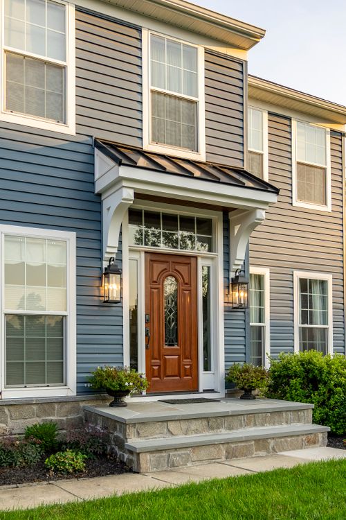 Front entry of a tan and blue colonial with a black metal awning and lantern sconces