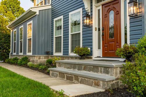 Stone entry steps and a landscaped bed beside a blue home's wood front door
