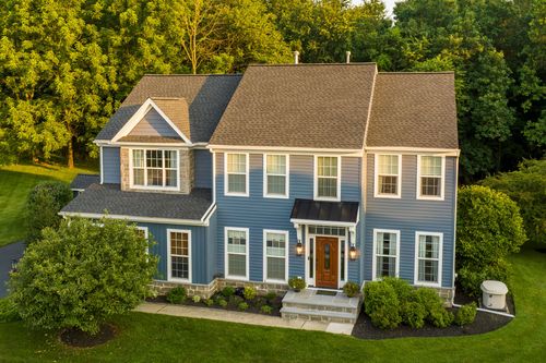 Aerial view of a blue two-story colonial with stone veneer and a wood front door