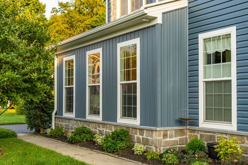 Blue board-and-batten siding with white-trimmed windows above a fieldstone base