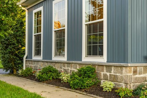 White-trimmed windows on blue siding above a fieldstone foundation and landscaping