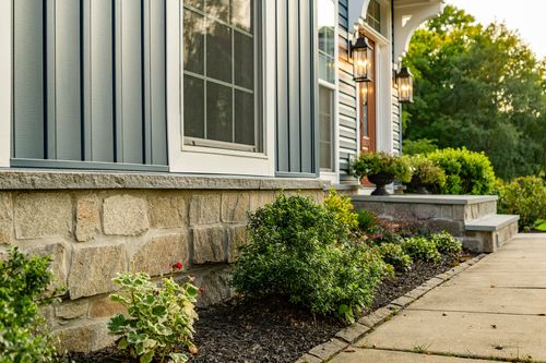 Stone foundation and a landscaped bed beside a covered front entrance