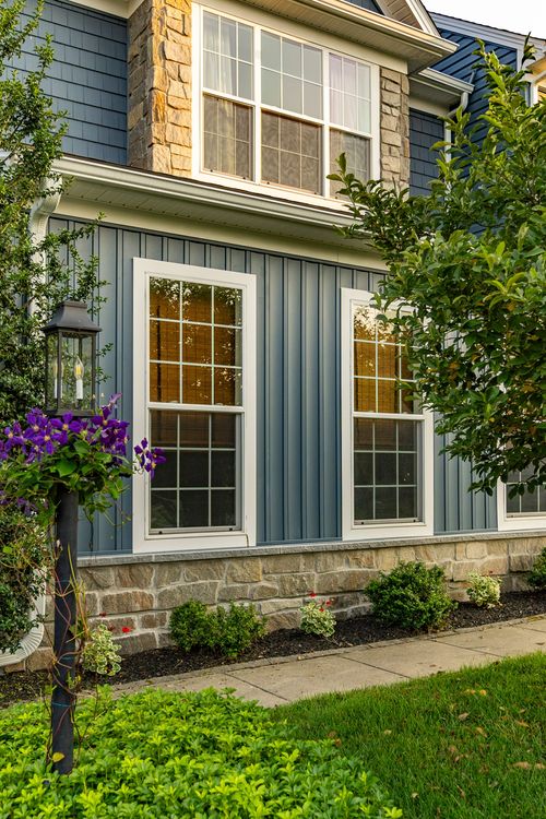 Dusk view of a blue two-story home with a stone-clad dormer and tall windows