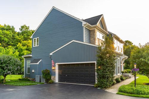Side elevation of a blue colonial with an attached garage and American flag