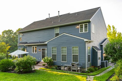 Rear elevation of a blue two-story home with a deck and manicured lawn at dusk