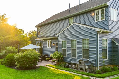 Rear elevation of a blue home with a covered patio and stone walkway at golden hour