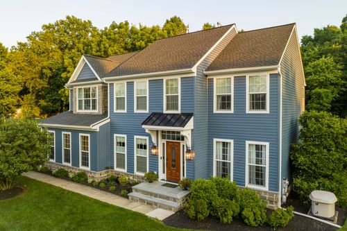 Aerial view of a blue colonial home with a stone base and manicured landscaping