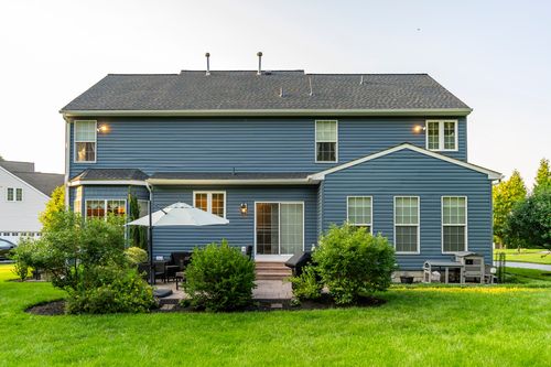 Rear elevation of a blue two-story home with a sunroom and patio at golden hour