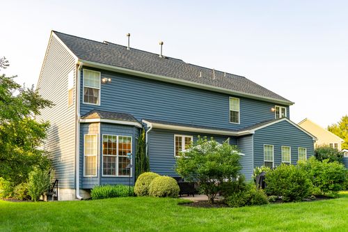 Rear elevation of a blue two-story home with a bay window in evening light