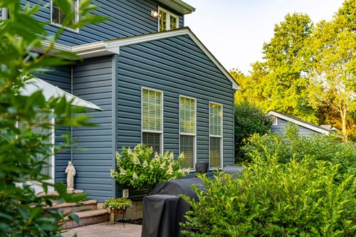 Rear elevation corner of a blue home with tall windows and shrubs