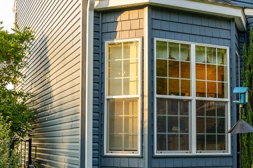Bay window detail with white trim on blue shingle siding at golden hour
