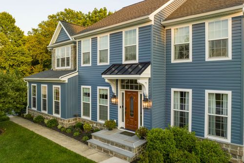 Front elevation of a blue two-story colonial with stone accents and a covered entry