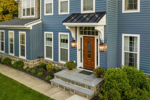 Front entrance of a blue home with a black standing-seam metal awning and stone steps