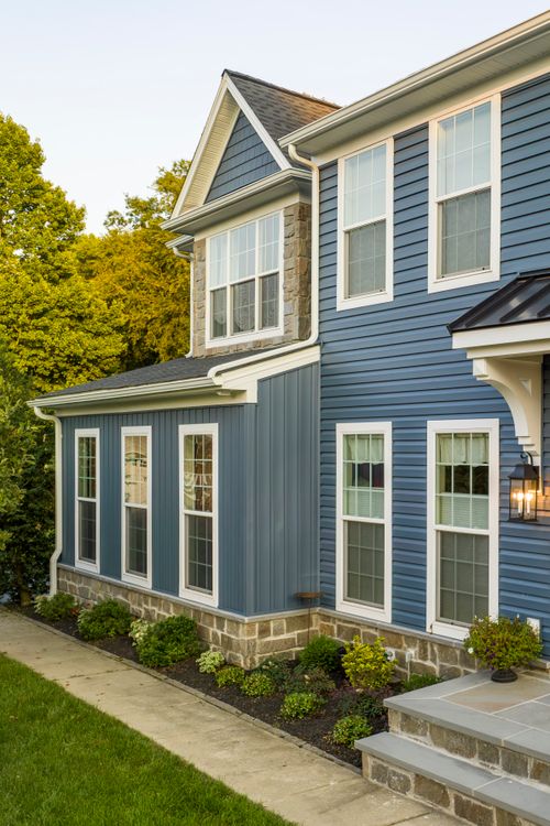 Black standing-seam metal entry awning above a wood door flanked by lantern sconces