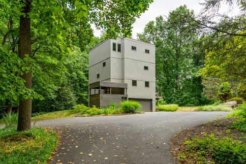 Modern gray tower-style home surrounded by trees at the end of a paved driveway