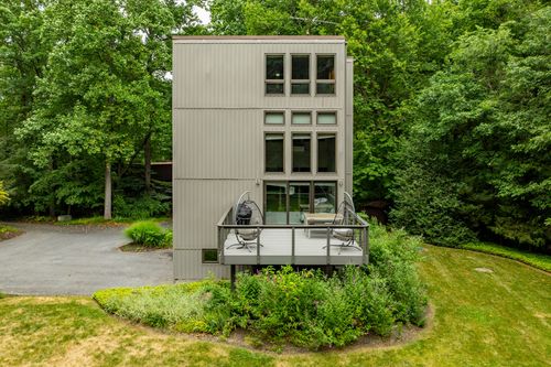 Aerial view of a modern vertical home with a deck surrounded by lush green forest