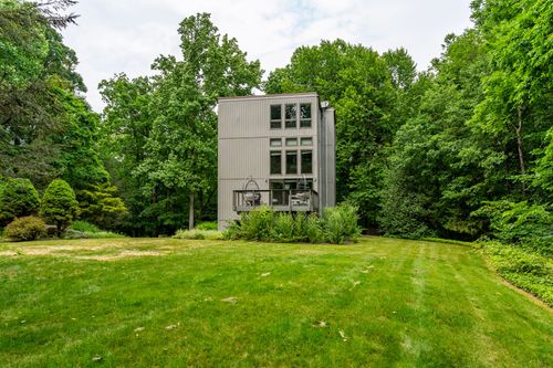 Rear elevation of a modern tower home framed by open lawn and dense woodland