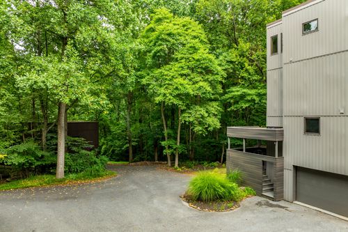 Gravel driveway winding through a wooded property beside a modern gray home