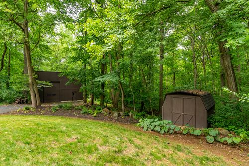 Dark wood outbuilding tucked into a wooded hillside beside the driveway