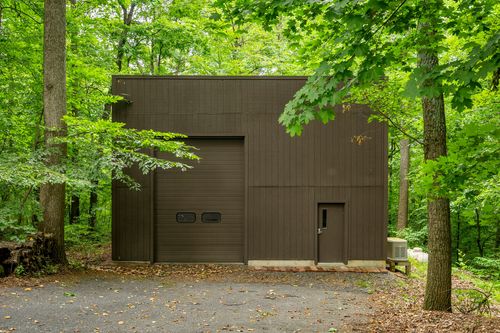 Exterior of a brown metal-sided outbuilding tucked among tall trees