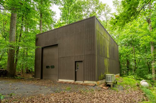 Dark brown metal outbuilding tucked among tall trees with a mossy roof