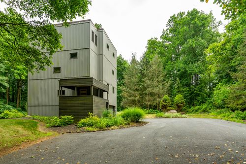 Modern gray tower home viewed from the circular driveway among tall trees