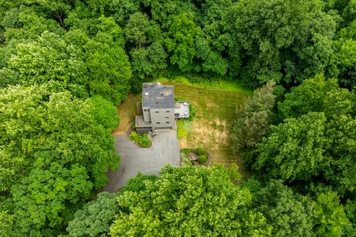 Aerial view of a gray modern home with a driveway carved into surrounding woodland