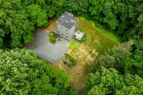 Aerial view of a gray tower home with a driveway loop deep in wooded acreage