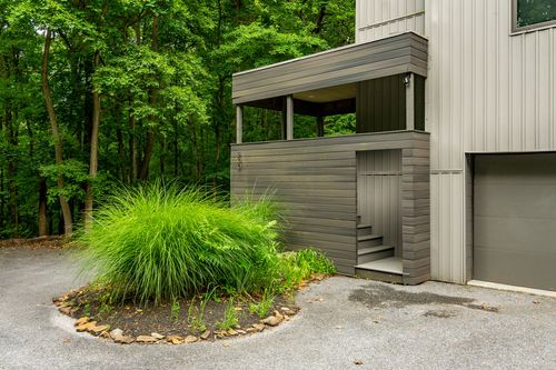 Covered side entrance with slatted wood walls, steps and ornamental grass