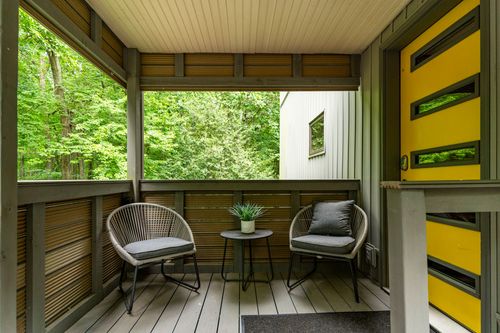 Covered porch with woven wicker chairs, wood slat walls and a mustard yellow front door
