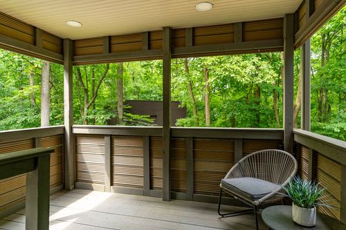 Screened porch with wood slat privacy walls, a small side table and wooded backyard view